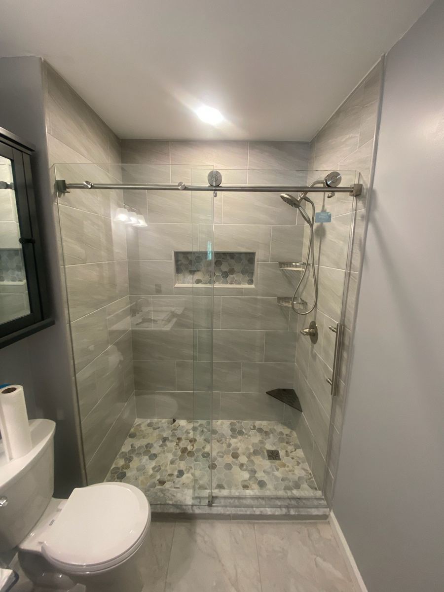 Bathroom after remodel: tiled walk-in shower with glass slider and pebble floor