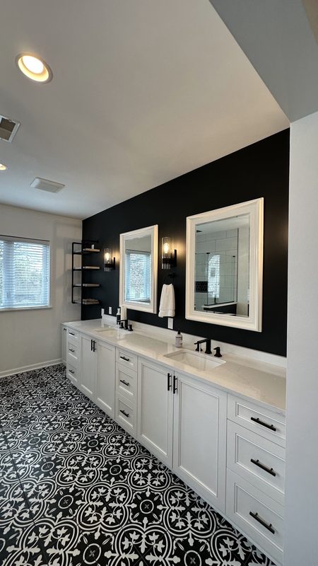 Remodeled bathroom with white double vanity, black accent wall, framed mirrors and black-and-white patterned tile floor
