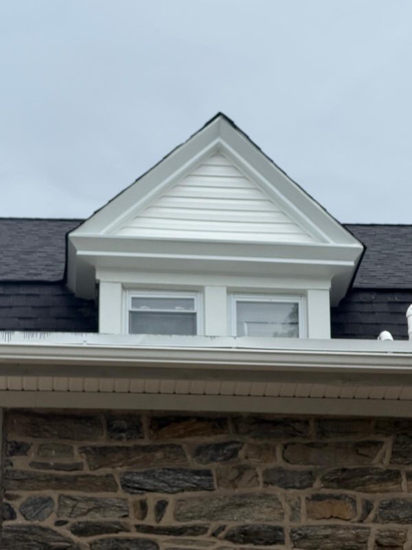 Front of a stone house with a new white-trimmed dormer and new dark shingles