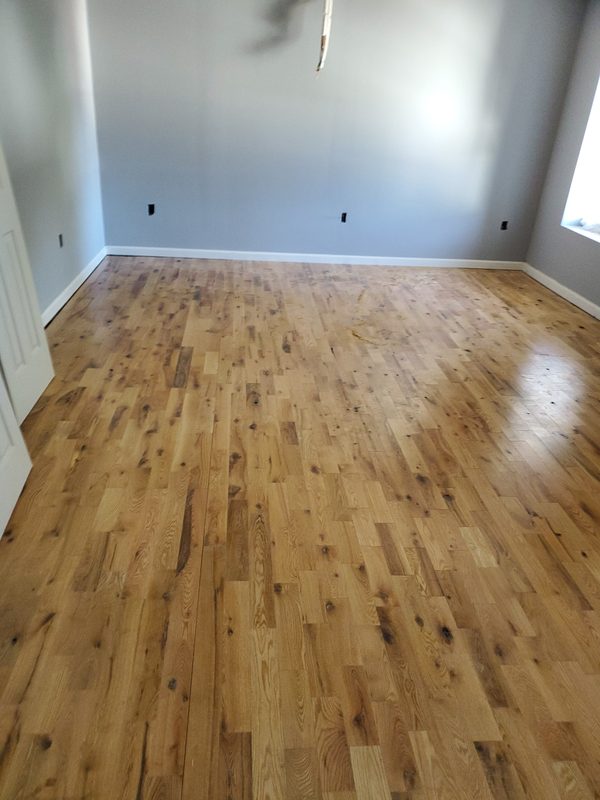 Empty room with newly finished natural oak hardwood floor and fresh white trim