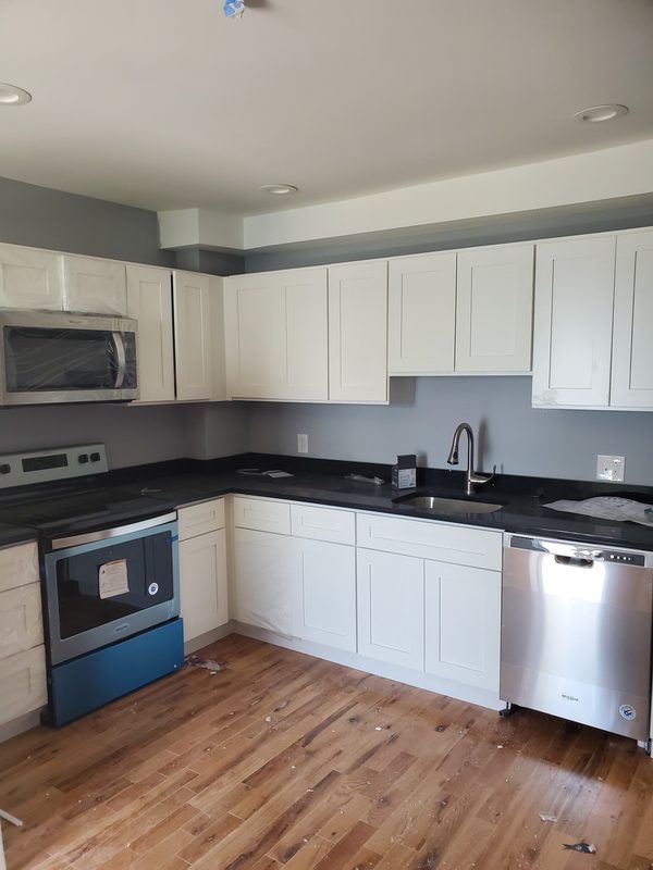 Finished kitchen with white cabinets, dark countertops, stainless appliances and wood floors